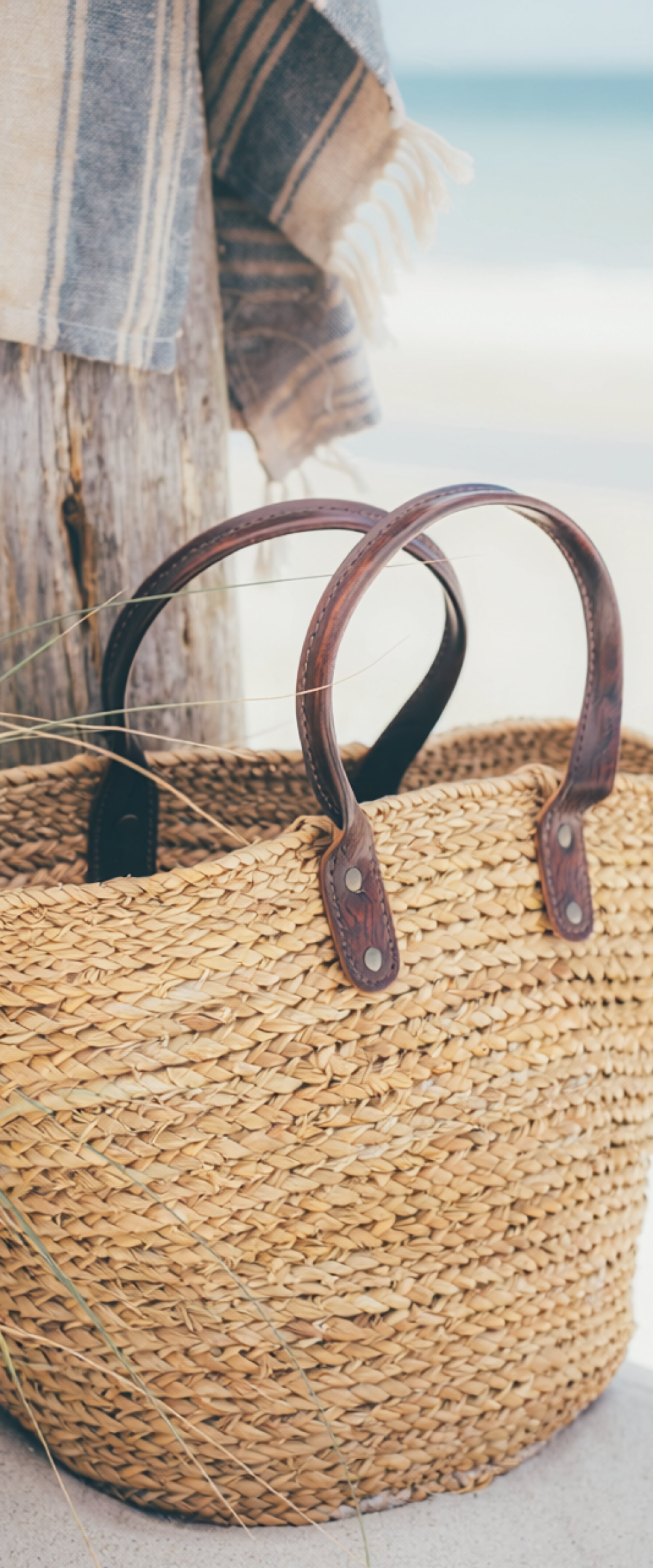 Banner décoratif Bain de soleil - Panier de plage en osier naturel avec anses en cuir marron sur ponton en bois, vue sur mer turquoise