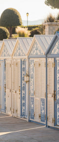 Banner décoratif Cabines de bain - Cabines de plage blanches et bleues avec volets persiennes, toits ajourés et jardin méditerranéen, ambiance Côte d'Azur