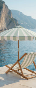 Banner décoratif Italian coast - Transat en bois rayé beige et blanc avec parasol vert sauge sur ponton face à la mer turquoise, ambiance Côte Amalfitaine