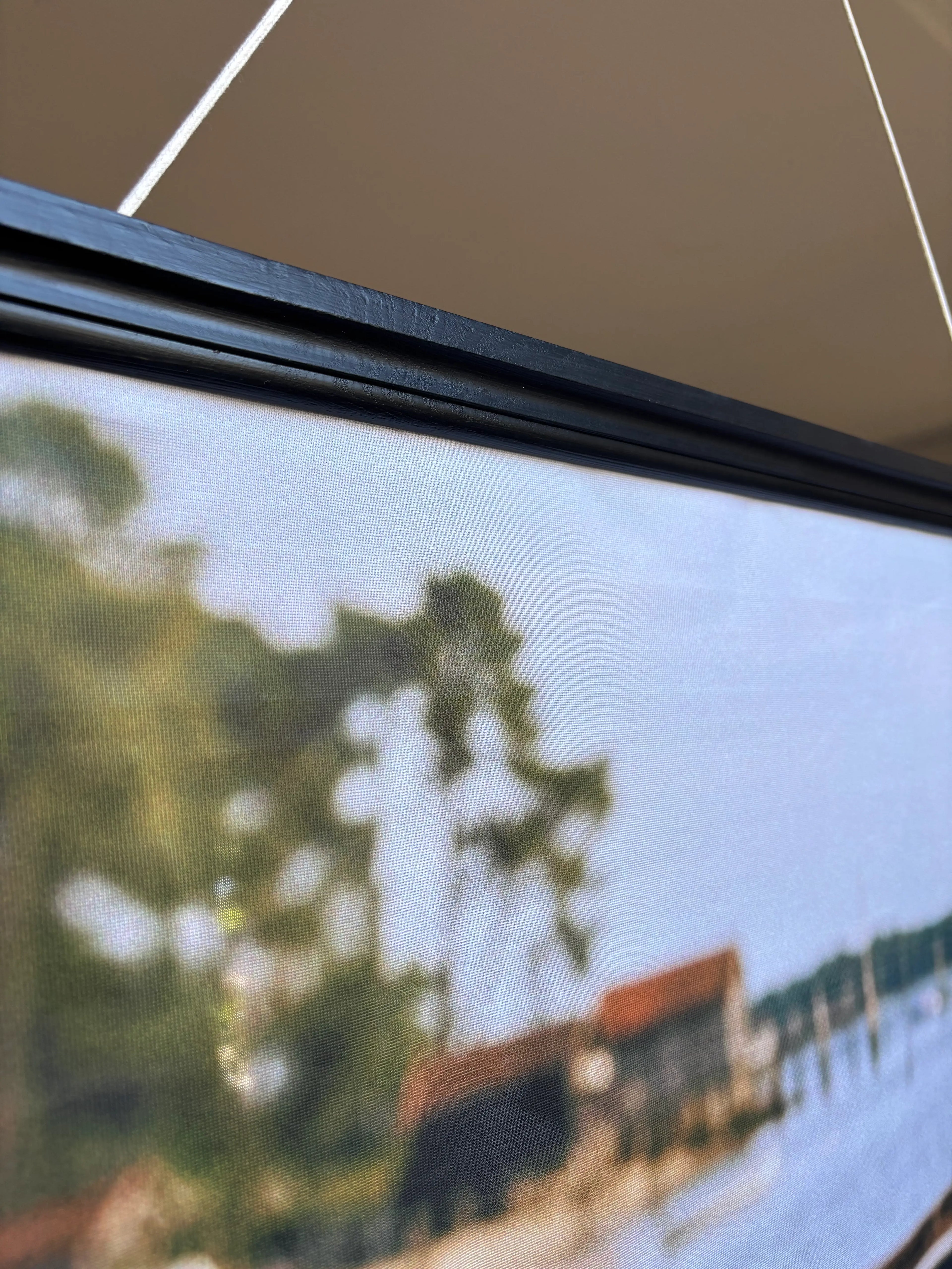 Banner décoratif Bateau de pêche - Vue banner suspendu avec barre fixation noire, paysage lacustre avec arbres, toits rouges et plage, toile semi-transparente microperforée