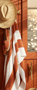 Banner décoratif Escale dorée - Intérieur cabine yacht bois acajou avec patère laiton, chapeau panama, serviette rayée terracotta et blanc, espadrilles, reflets dorés mer, ambiance luxe nautique