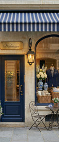 Banner décoratif Boutique chic - Façade boutique parisienne avec porte bleu marine, store rayé, vitrine élégante avec costume et pivoines blanches, ambiance luxe