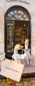Banner décoratif Oies fanchon - Deux oies décoratives avec tutus et sacs shopping Vitrines Fanchon devant porte cintrée noire, mur briques, hortensias blancs, ambiance boutique chic